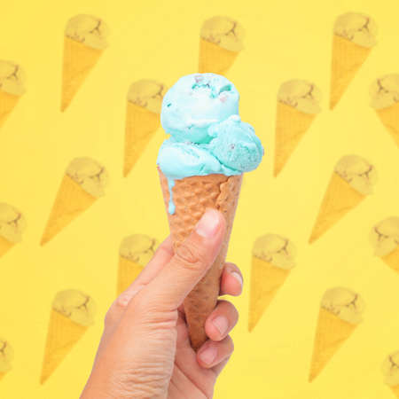 woman hand holding wafer cone with blue  ice cream on pattern background