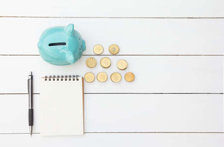 Piggy saving with pile coin of Thai Baht and paper report,pen on white wooden table financial concept.Copy space for your textの写真素材