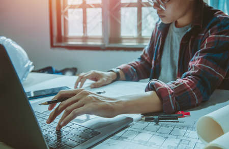 Engineering Asian man architects holding pencil working On laptop with a blueprint.Selective Focusの写真素材