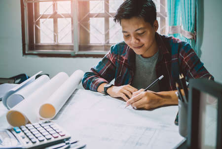 Asian man smiling and using pencil designer drawing renovation house plan equipment  architects On the desk with a blueprint in the office. Vintage tone Selective Focusの写真素材