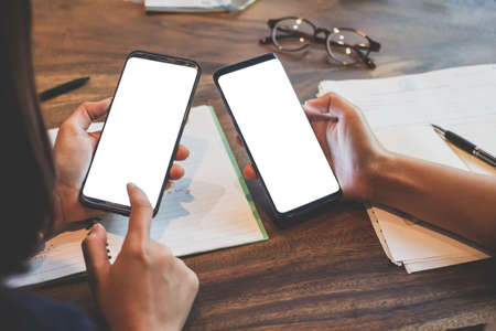Close up of woman hands holding touching mobile phone with blank copy space white screen for your text message and glasses,books in cafe with light Sunset,Vintage tone.Selective focusの写真素材