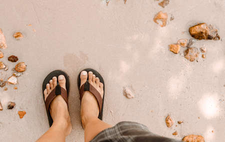 Blurred man in Black slippers  flip flop feet standing on the beach with a wave of foaming gentle...