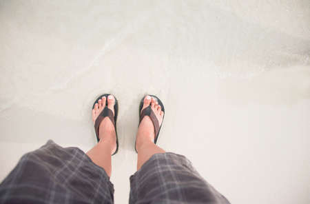 man in Black slippers  flip flop feet standing on the beach with a wave of foaming gentle beneath them.Top viewの写真素材