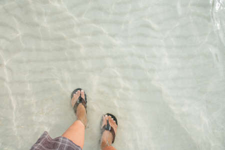  Top view legs in black flip flop underwater of sea on the beach with white wave sand. vacation summer in a holidayの写真素材