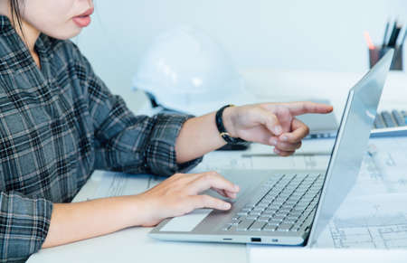 Woman designer architect sitting and pointing drawing project working on laptop with a blueprint and...