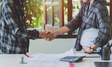 Architects work together to build good relationships, shake- hands, and together as a team, planning and constructing buildings for work. There are plans and blueprints on the table.の写真素材