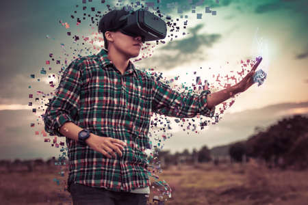 Asian man in tartan shirt wearing glasses of virtual reality dissolving into pixels on outdoor. Future Technology Conceptの写真素材