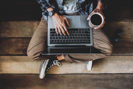 businessman  holding coffee cup sitting on wooden floor with glasses using laptop working at home to send and send reply to email Message customer serviceの写真素材