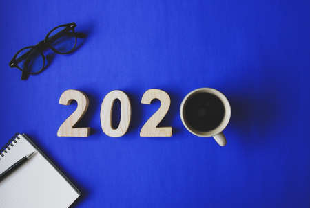 Concept celebrate New year 2020. business food drink cup of coffee with glasses, pencil and notebook on blue paper background. Top viewの写真素材