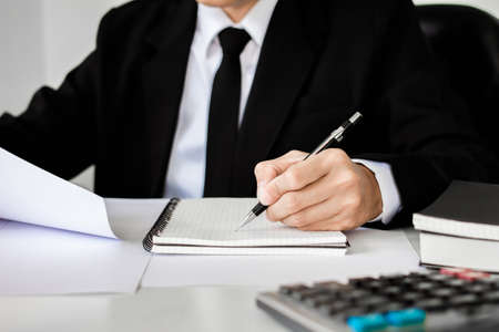 Writing paper on desk, businessman hand using calculator Calculating bonus(Or other compensation) to...