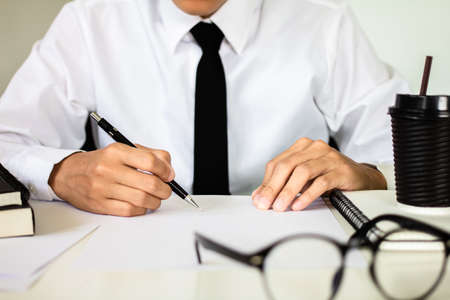 Businessman hand holding a pen writing notebook working on table at the officeの写真素材