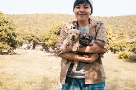 Happy Asian owner carrying, hug adorable puppy dog on her Stand on the grass backyard lawn