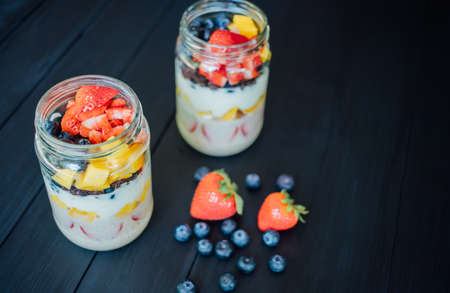 Overnight oats with fresh Fresh sliced mango blueberries and strawberries fruit in a glass jar on wood table. Breakfast or healthy food concept, Top view photoの写真素材