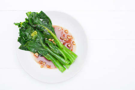 Fried kale, oyster oil with fried garlic in a plate On a white wood table background,Copy space for your text. Top viewの写真素材