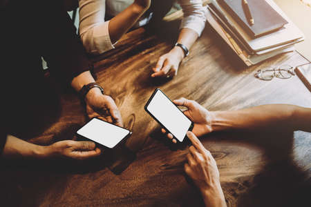Soft focus men and woman hands holding touching mobile phone with blank copy space white mock-up for your text message on wooden table in a cafe with light Sunset, Vintage tone. Soft focusの写真素材