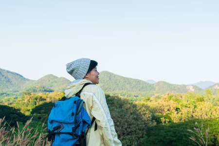 Asian young man in a yellow long shirt and gray hat hiking standing smiling and happy at green mountain peak above clouds Hiker outdoor. Lamphun Province, In the morning.の写真素材