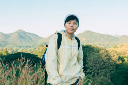 Asian young man in a yellow long shirt and gray hat hiking standing smiling and happy at green mountain peak above clouds Hiker outdoor. Lamphun Province, In the morning.の写真素材