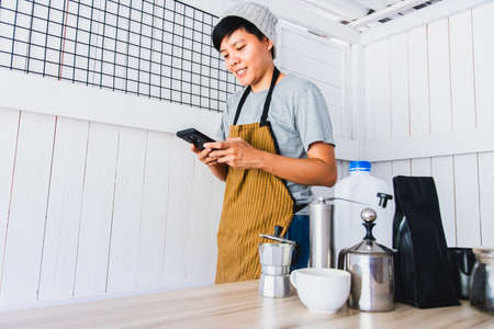 coffee shop owner smile using a phone order to confirm the coffee menu order. Ordering food and beverages online via social media, Transport delivery. There are coffee percolator and coffee toolsの写真素材