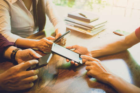 Soft focus men and woman hands holding touching mobile phone with blank copy space white mock-up for your text message on wooden table in a cafe with light Sunset, Vintage tone. Soft focusの写真素材