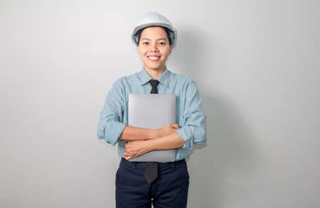 Smile asian engineer wearing a helmet with laptop standing on grey background
