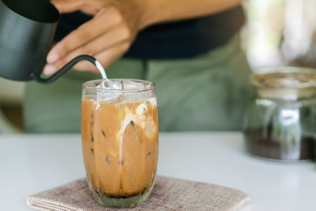 Hand of a barista pouring milk makes iced coffee on the table.の写真素材