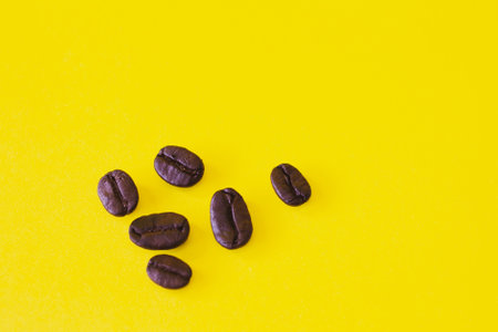 Six dark roasted coffee beans Arabica coffee beans on a background of yellow paperの写真素材
