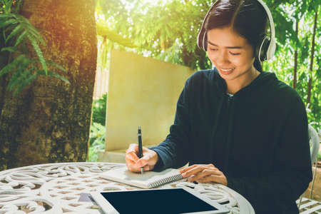 A smiling Asian woman sitting in a chair listening Online media education Through listening by wearing headphones to listen to improve listening skillsの写真素材