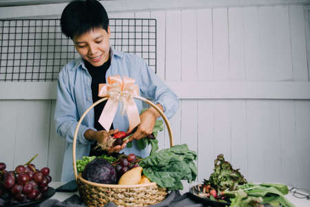 Enjoying aisan man in a blue shirt will prepare a basket of fresh vegetables, kale, potatoes, purple cabbage, and grapes. Gifts for your healthの写真素材
