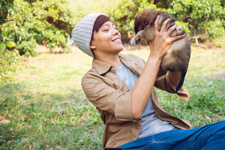 Happy Asian owner carrying, hugging Carrying adorable puppy dog her sitting green grassの写真素材