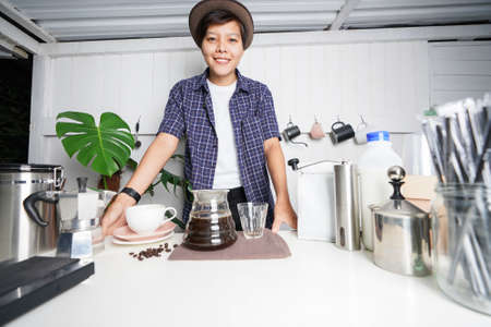 Small coffee shop business owner of 30s Asian lesbian wearing vintage hat smiling happily looking at the camera. And coffee jug Coffee equipment in a bar on white shop at home.の写真素材