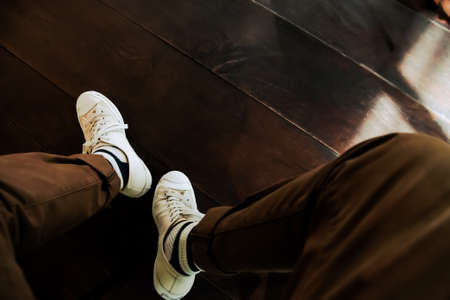 The casual young man is casual wearing white sneakers and brown pants sitting on a chair in a coffee shop.の写真素材