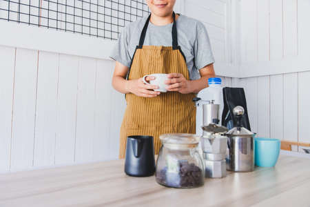 Smiling barista in brown apron is holding a cup of latte coffee in cafe shopの写真素材