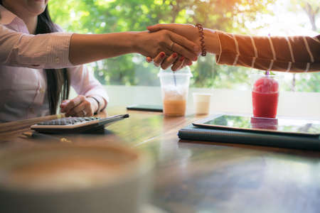 asian business woman staking hand, together create a mutually beneficial business relationship. Economic graph on tablet the table, Meeting point at the coffee shopの写真素材
