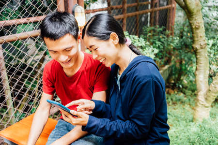 Smiling Asian couple have funny social media Internet on modern smartphone  watching online movie on a smartphone to his girlfriend at the cafeの写真素材
