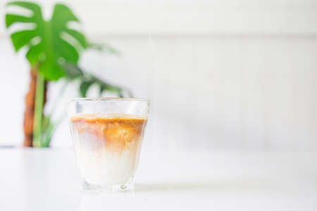 Menu coffee or dirty coffee with iced milk on top of a hot coffee on a white table with tree pot copy space for textの写真素材