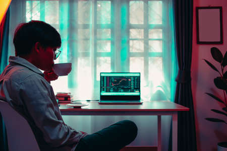 business Asian woman 30s looking graphs cryptocurrency trading platforms on laptop and drinking hot...
