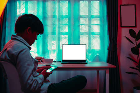 Selective focus doesn't focus on women LGBTQ business Asian man using smartphones calling friends with display white mockup digital laptop above the desktop table on colorful office worker at homeの写真素材