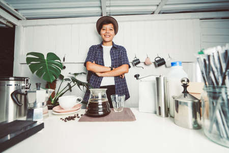 smiling young barista standing at his the bar counter workplace with a coffee jug and equipment make...