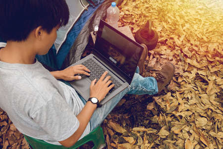 Asian Freelancer sitting on his laptop surfing the Internet to listen to his music and relax on the weekends. Take a break from camping alone on vacation.の写真素材