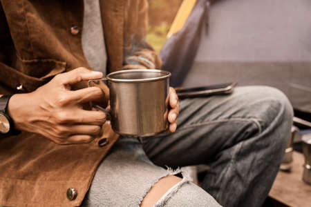 Happy asian lesbian holding hot espresso stainless steel with Italian Moka coffee pot drinking in a forest on vacation, traveler outdoor the tent happy single picnic camping on the morningの写真素材