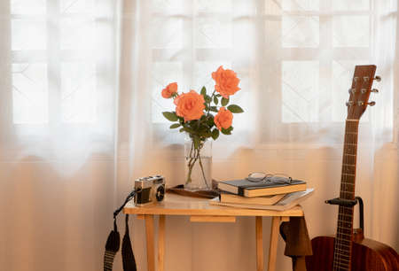Coral pink roses in a vase, on the table there are books and notebooks, eyeglasses. and a film...
