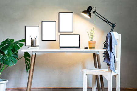 Home office with laptop mockup and chair, document book on table decor white frame as lamp light and monstera tree pot plants house nature wall modern loft interior decorations workspace.の写真素材
