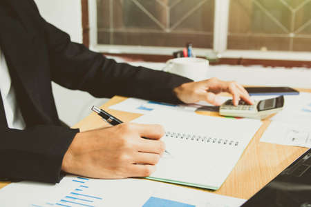 businessman hand using calculator Calculating bonus(Or other compensation) to employees to increase productivity. Writing report paper on the desk working from a home office. Selective Focusの写真素材