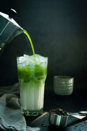 Poured Matcha green tea with Italian Moka pot pouring into a cup with iced of milk and powdered...