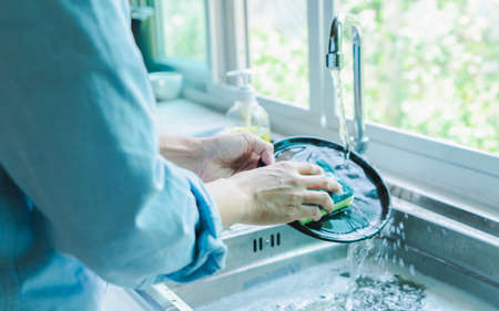 Close-up of a woman washing dishes with dirty food scraps Cleaner in the sink the kitchen counter at...