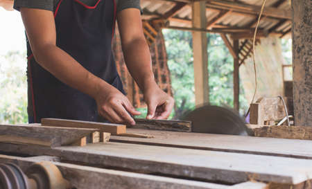 Asian carpenter is using a circular saw to cut wood to construct a storage box on a desk table at his factory. Working as your own boss at home conceptの写真素材