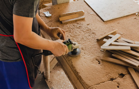 Asian carpenter is sanding wood using an electric wood sander to smooth the wood surface on a...