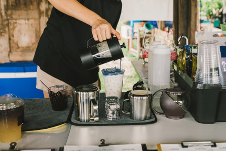 Young barista pouring concentrated butterfly pea flower water onto a glass prepared with ice. On the bar table, selling fresh coffee, cold drinks, herbs, water menus, preparations, coffee shop owner.の写真素材