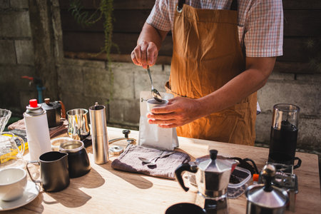 Barista is grinding coffee beans with manual stainless steel grinder to make black coffee machine, brewing equipment or coffee drip set Dripper on a wooden table In the kitchen at home in the morning.の写真素材