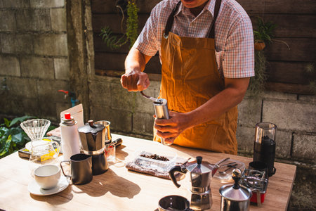 Barista is grinding coffee beans with manual stainless steel grinder to make black coffee machine, brewing equipment or coffee drip set Dripper on a wooden table In the kitchen at home in the morning.の写真素材